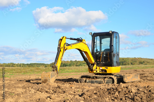 Mini excavator digging earth in a field or forest. Laying underground sewer pipes during the construction of a house. Digging trenches for a gas pipeline or oil pipeline. Earthwork, foundation pit