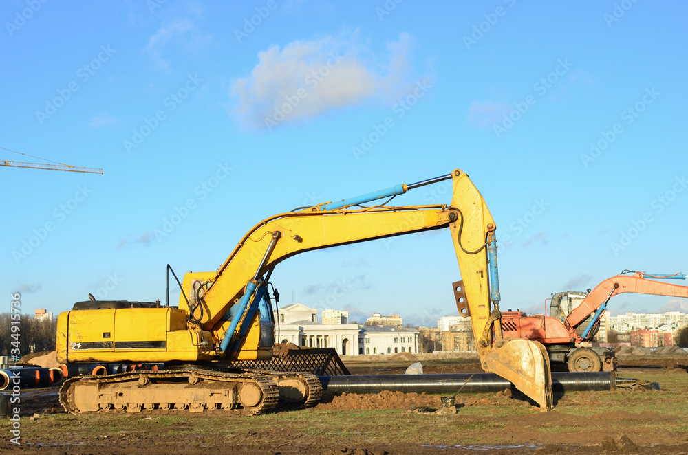 Excavator with a large iron bucket on a construction site during road works. Backhoe dig the ground for the foundation, laying storm sewer pipes. Installation of water main systems. Small sharpness Excavator with a large iron bucket on a construction site during road works. Backhoe dig the ground for the foundation, laying storm sewer pipes. Installation of water main systems. Small sharpness