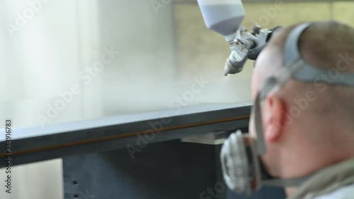 Man spraying varnish on a piece of furniture in a painting chamber