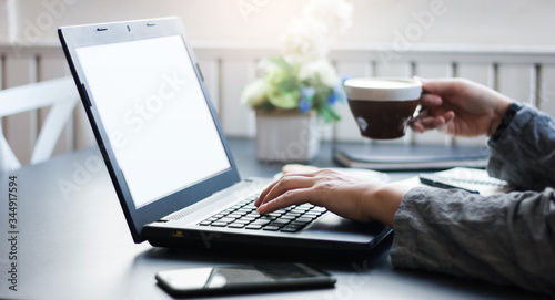 Close-up of  businesswoman using laptop and smartphone working online at home and holding coffee cup to drink, Concept work from home