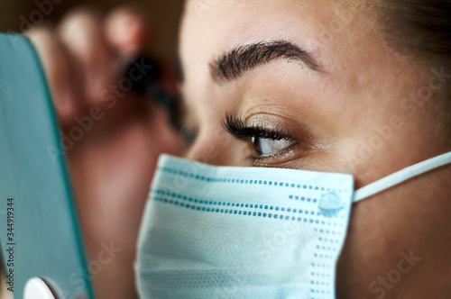 Beautiful Women paints lashes In A Medical Mask. Close-up of a young girl with a surgical mask on her face