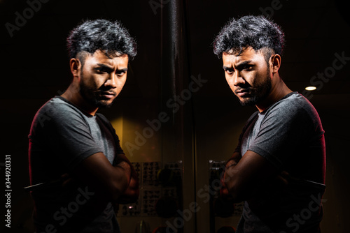 Portrait of black Asian man with beard short hair wear grey shirt shave facial by razor looking reflection in mirror on fitness background stock photo