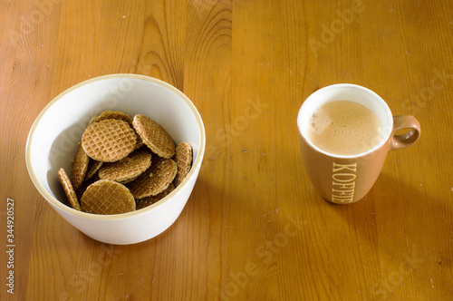 Bowl of mini stroopwafels and a cup of coffee on a wooden table. A stroopwafel is a traditional dutch cookie . Translation: koffie means coffee photo