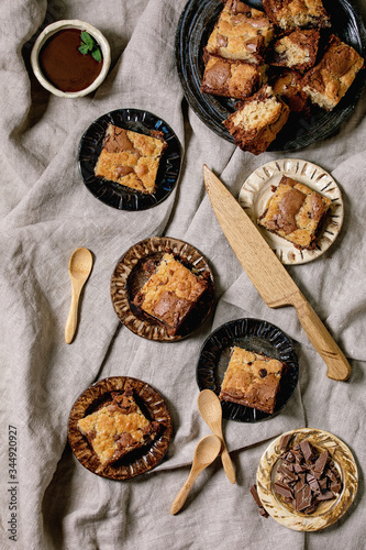 Fototapeta Naklejka Na Ścianę i Meble -  Trend baking Brookies chocolate brownies and cookies homemade cake sliced by squares in different ceramic plates, chocolate sauce, wooden spoons on grey linen cloth background. Flat lay, space