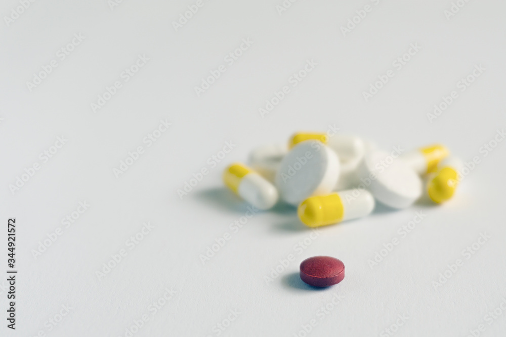 one red pill with many white and yellow pills on white background. copy space one red pill with many white and yellow pills on white background. copy space