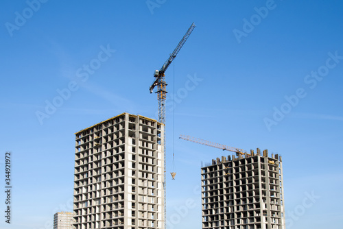 Tower cranes working at construction site against blue sky. Crane lifting a concrete bucket. Construction process of the new residential buildings. Transportation blocks and pouring of the cement mix