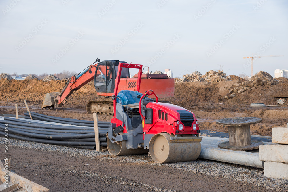 Obraz premium Road roller and excavator working at construction site during asphalt road repair. Paving roller machine on paving works.