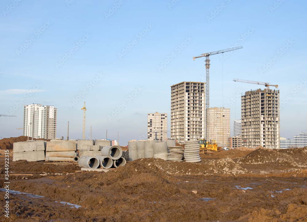 Tower cranes working at construction site on blue sky background. Laying concrete manholes and drain pipes for stormwater system. Construct stormwater and underground utilities