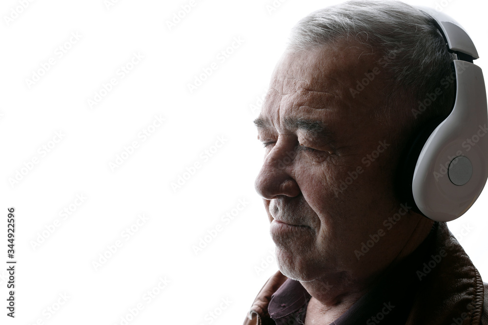 Fototapeta premium Portrait of old man in headphones listening music with closed eyes. White background. Free space for text.