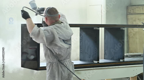 Man spraying varnish on a piece of furniture in a painting chamber
