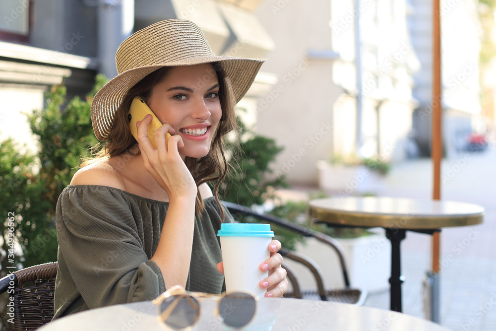 Attractive laughing woman talking on cellphone while sitting in cafe outdoors.