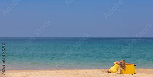 Beautiful girl in a yellow dress on the beach with a yellow suitcase. Blue sea. Yellow sand