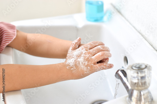 Little girl use soap and washing hands with running water tap. Hygiene concept.