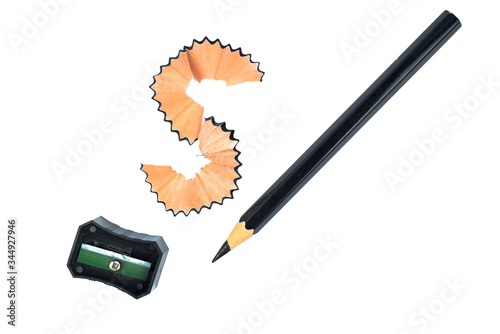 A black color wood pencil crayon placed beside a s shaped pencil shavings and a sharpener