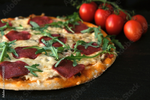 homemade pizza on a dark rustic background, next to a branch of tomatoes and arugula greens.