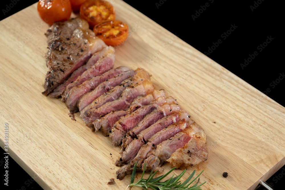 Slice Juicy grilled steak medium rare beef on wooden cutting board with tomato and rosemary , black background  - Stock photo