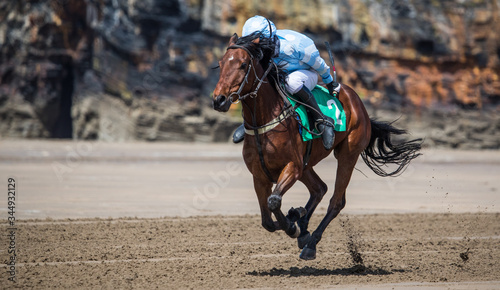 Single race horse and jockey racing on sandy beach