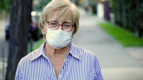 Beautiful old lady looking at camera and wearing a protective mask in the street