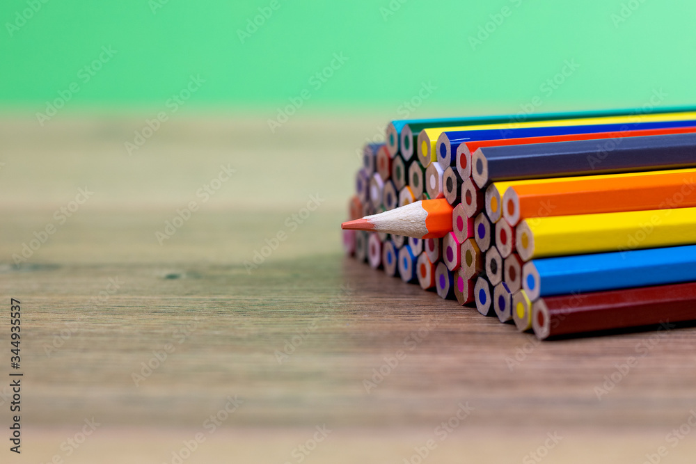 close up view of colored pencils stacked with an orange pencil turned upside down spilling out
