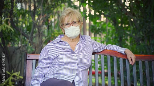 Mature woman wearing a protective mask and sitting in the garden due to covid-19 preventive measures