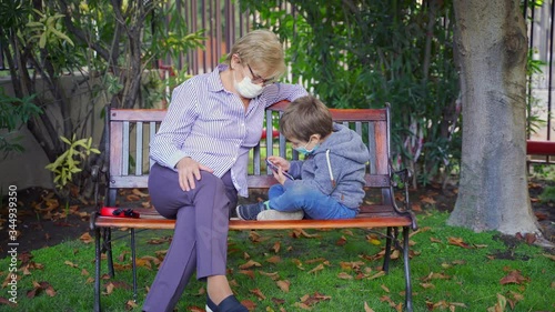 Grandmother playing games with her grandson in the back garden and wearing protective masks