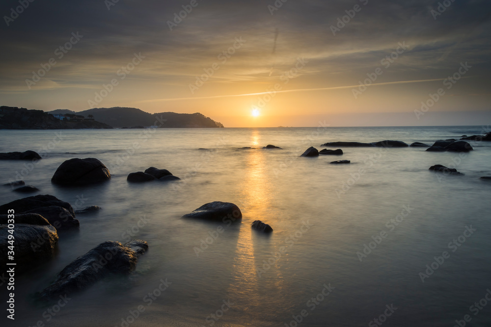 Sun on the horizon of a beach with rocks