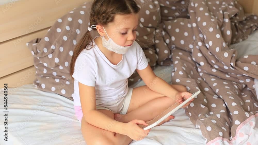Little girl in a respiratory mask sits in quarantine in tablet Little girl in a respiratory mask sits in quarantine in tablet