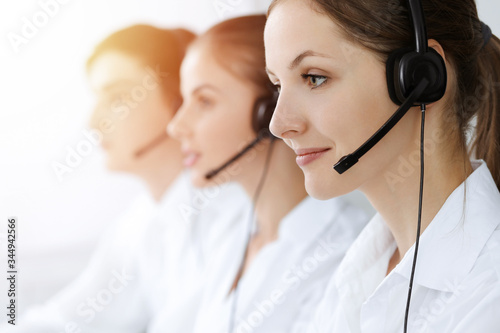 Call center. Beautiful young woman using headset and computer to help customers in sunny office. Business concept