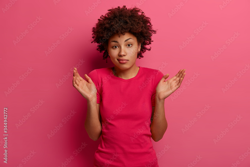 People, lifestyle, perception concept. Questioned bewildered Afro American woman stands unsure, shrugs shoulders, cannot give answer on difficult question, has perplexed expression, stands indoor