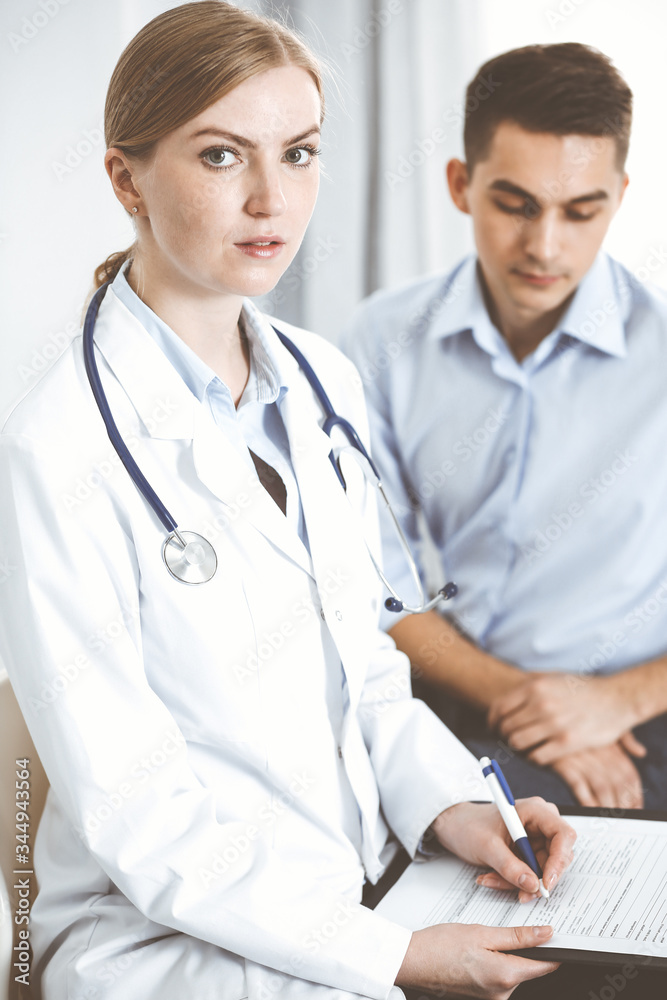 Female doctor holding application form while consulting man patient in hospital office. Medicine and healthcare concept Female doctor holding application form while consulting man patient in hospital office. Medicine and healthcare concept