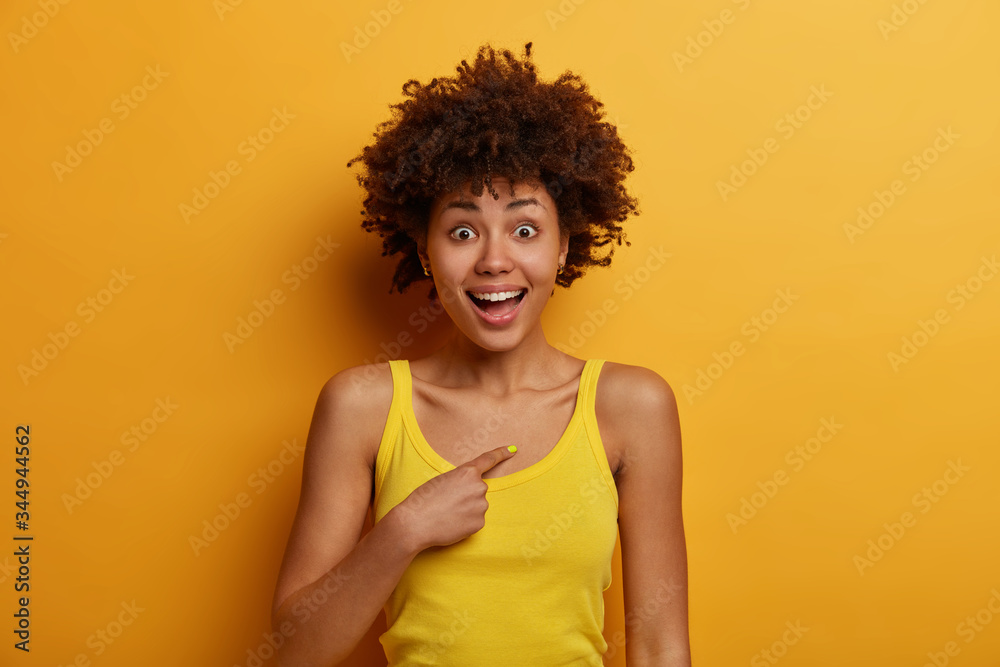 Unbelievable, really me? Surprised glad dark skinned woman points at herself, shocked and happy to hear her name or being chosen, becomes team member, dressed in casual clothes, poses over yellow wall Unbelievable, really me? Surprised glad dark skinned woman points at herself, shocked and happy to hear her name or being chosen, becomes team member, dressed in casual clothes, poses over yellow wall