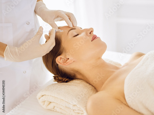 Beautiful woman receiving beauty injections with closed eyes. Beautician doctor hands doing beauty procedure to female face with syringe