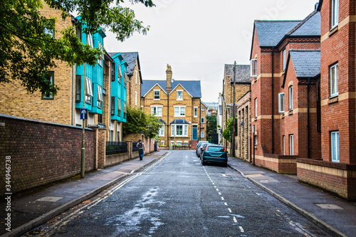 Oxford UK street with cars parked and tall buildings on either side and wet pavement and young may with backpack walking on sidewalk  - sign reads Rickmond Road