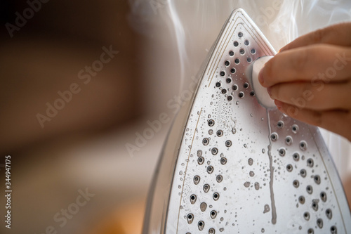 Close-up. A woman is cleaning the surface of a heated iron with a special pencil tool. Technology and service. photo