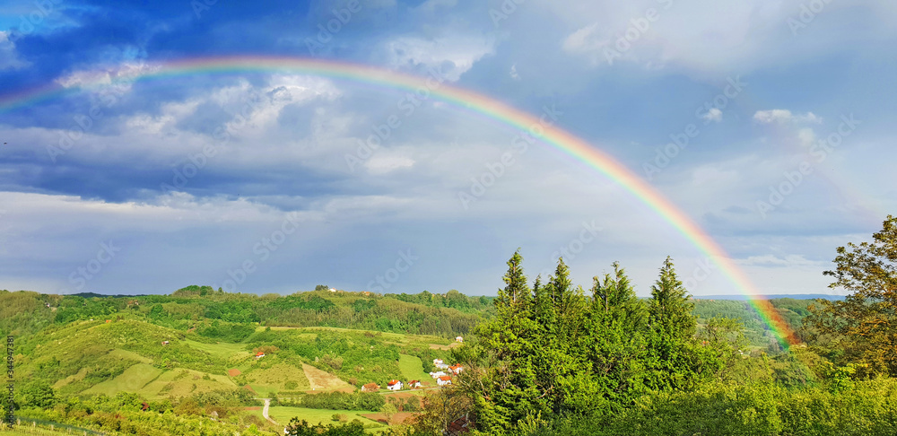 Fototapeta premium Spring rural rainbow landscape, view of green meadows and hills