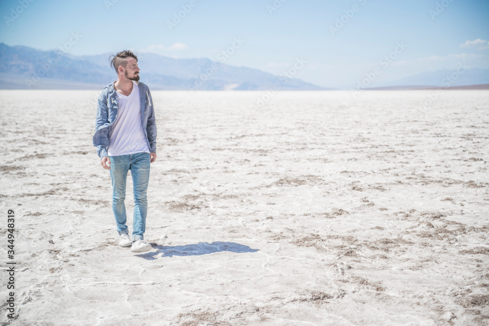 young male traveler walking across badwater basin in death valley national park