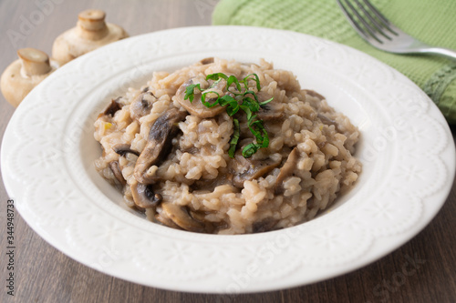 Classic Italian vegan mushroom risotto made with arborio rice, mushrooms, onion and garlic garnished with basil ribbons on a rustic wooden surface with a green napkin and a fork