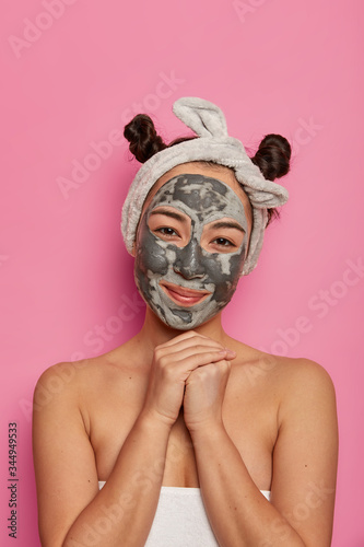 People, skin care and spa treatment concept. Satisfied female model keeps hands under chin, applies face mask for perfect pure skin and reducing wrinkles, stays fresh and young, keeps healthy hygiene