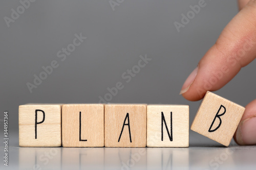 Wooden cubes with the word Plan B on grey background and human finger, business concept background