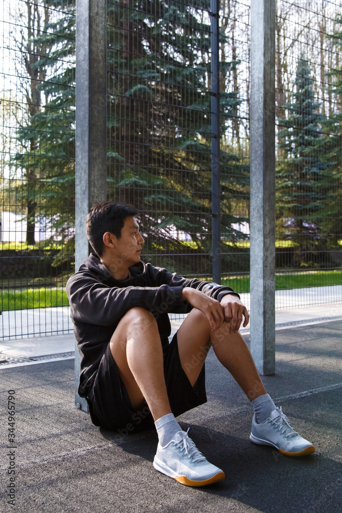 Asian athlete resting near fence on sports ground Asian athlete resting near fence on sports ground