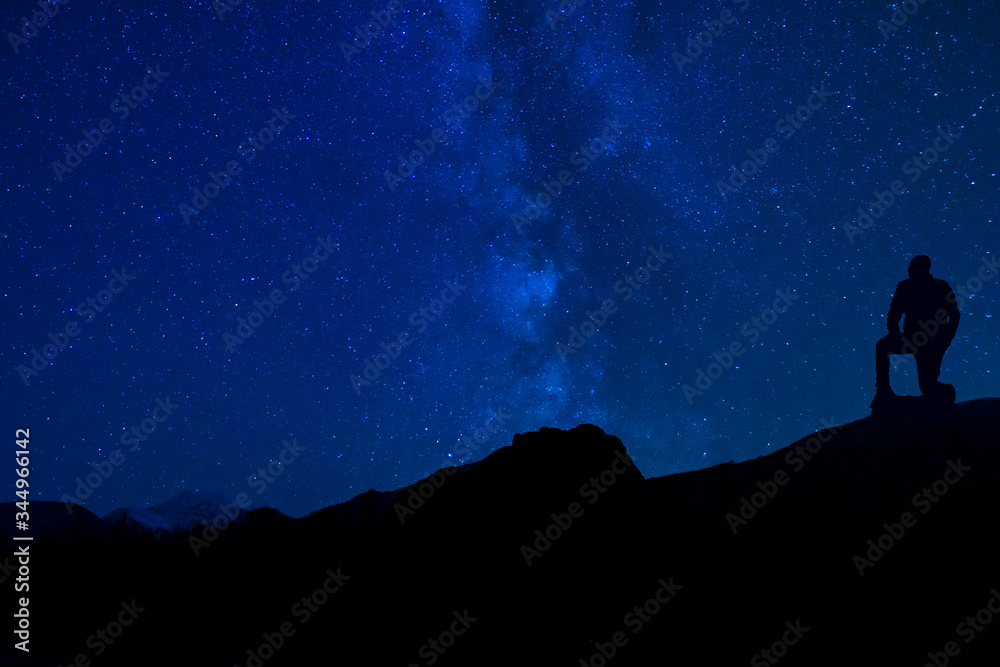 Man Kneeling To Pray Under Stars At Night Sky
