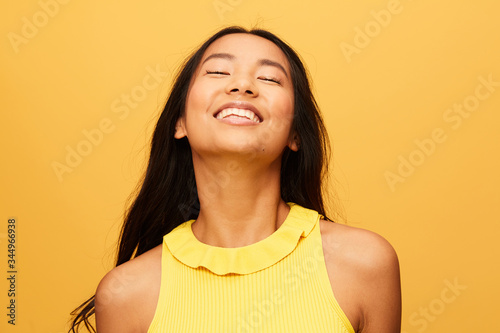 Happy asian Woman portrait with eyes closed laughing isolated over yellow