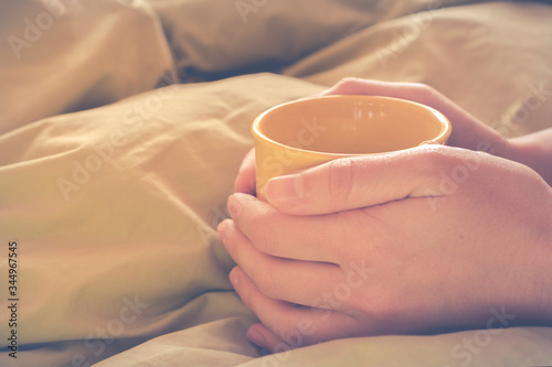 Woman hands having a cup of tea with teabag on yellow bed comforter