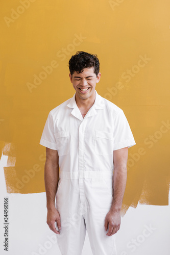 super happy young man wearing white painters outfit in front of gold painted wall
