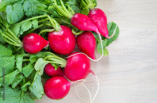 close up of ripe red radishes with leaves and stems on a wood background with copy space