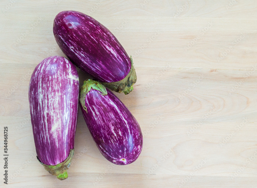 three fresh purple and white striped graffiti eggplants on a wood background with copy space three fresh purple and white striped graffiti eggplants on a wood background with copy space