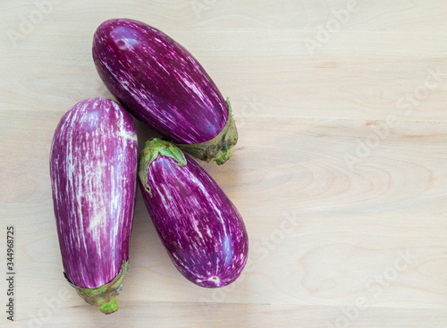 three fresh purple and white striped graffiti eggplants on a wood background with copy space