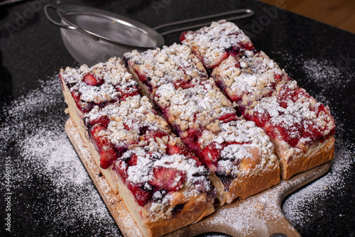 strawberry yeast cake covered with powdered sugar on wooden board