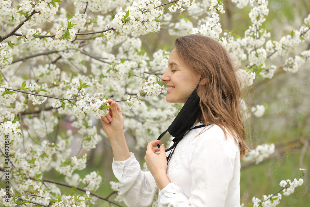 happy beautiful girl took off her medical mask to breathe in the smell of flowers. A girl in a mask stands in blossoms. the end of quarantine happy beautiful girl took off her medical mask to breathe in the smell of flowers. A girl in a mask stands in blossoms. the end of quarantine