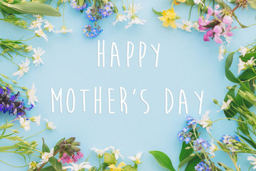 Happy Mother's day greeting card. Heart of colorful spring flowers  on blue background flat lay with greeting text. Floral greeting card. Happy Mothers day stylish flat lay